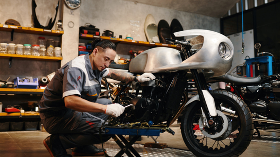 工具を持ちながらバイク整備を行う整備士と整備現場の様子。